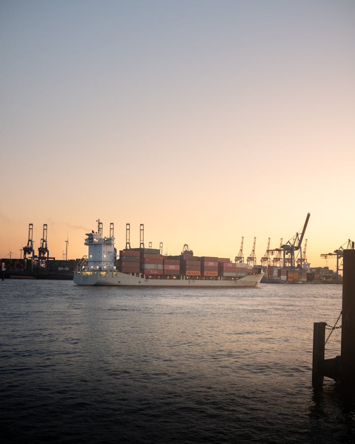 A container ship sails through Hamburg harbor at sunset, capturing industrial beauty.
